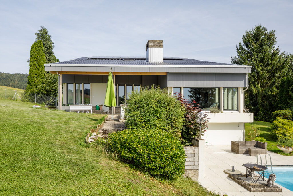 Das Bild zeigt ein modernes Einfamilienhaus mit grosser Terrasse, Pool und gepflegtem Garten in ländlicher Umgebung.