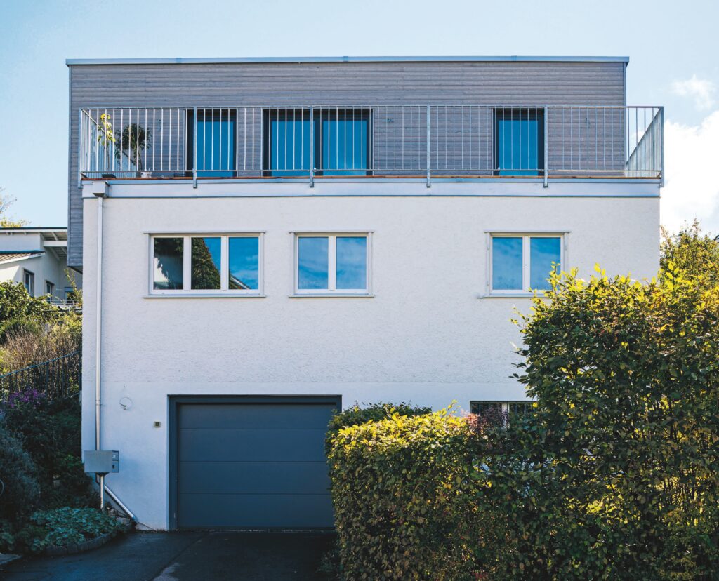Das Bild zeigt die Rückseite eines modernen Wohnhauses mit Flachdach, Balkon, Garage und klar strukturierter Fassade.