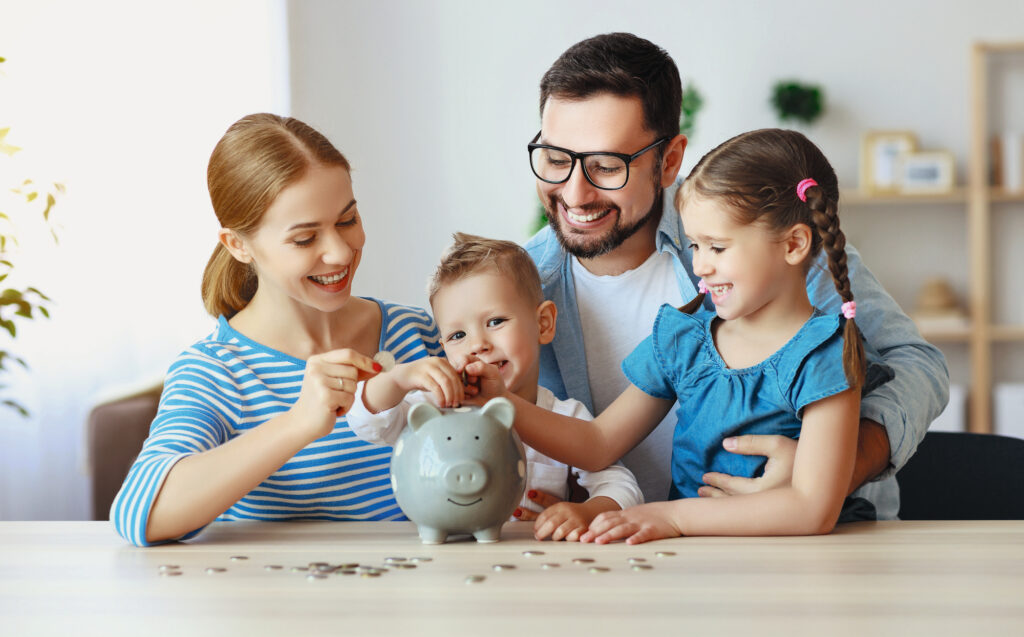 Das Bild zeigt eine glückliche Familie, die gemeinsam Geld in ein Sparschwein legt und dabei lächelt.
