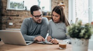 Mann und Frau sitzen am Tisch mit Laptop und Dokumenten und besprechen sich